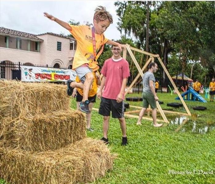 Young boy jumping off hay barrels in obstacle course