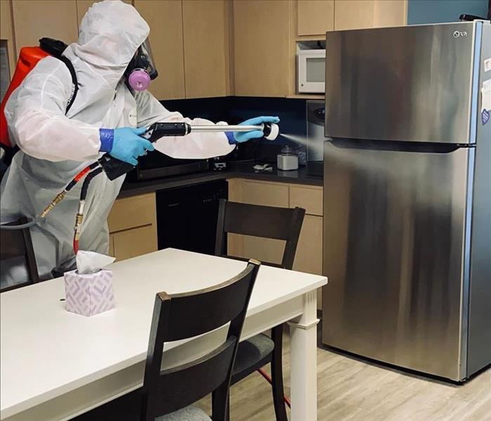 man wearing white tyvek suit spraying a fridge with disinfectant